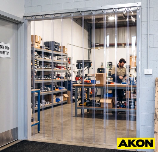 Reusable vinyl PVC strip curtain hanging in an industrial doorway to separate work areas.