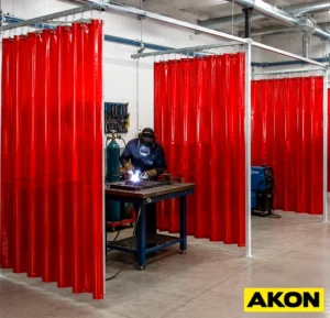 Transparent amber welding curtains hanging in an industrial workspace to contain sparks and shield nearby workers.