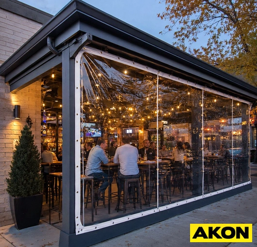A bar patio enclosed with clear vinyl tarps, keeping the space open and visible while string lights illuminate the fall setting.