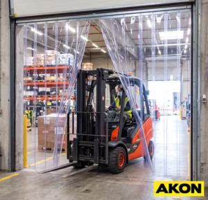 Clear PVC strip curtains hanging in an industrial doorway, allowing visibility and passage while separating work areas.