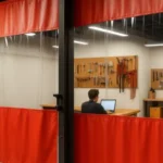 Makerspaces and Hackerspaces curtains with red vinyl and clear panels dividing a workshop, showing a person working on a laptop at a desk surrounded by tools and equipment