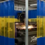 Blue and yellow plasma burn table enclosure with welding curtains containing sparks during cutting, Plasma Burn Table Enclosures Containment with Welding Curtains