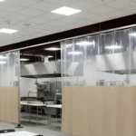 Curtain Walls for Blocking Off Cafeteria Equipment During Non-Use Hours, clear PVC with beige lower panels dividing the kitchen from the dining area