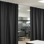 Curtain Walls for Blocking Off Cafeteria Equipment During Non-Use Hours, dark fabric panels partially open to reveal stainless kitchen equipment