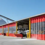 Exterior view of Curtain Walls for City Public Works Yards and Salt Dome Storage Areas showing red partitions enclosing municipal trucks and plows near a salt dome