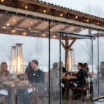 Snow-covered café patio protected by transparent vinyl walls for cozy winter dining Extend Patio Season Restaurant and Café Enclosure Ideas For Winter