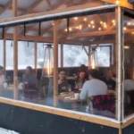 Warm and inviting café enclosure with vinyl walls and string lights in snowy weather Extend Patio Season Restaurant and Café Enclosure Ideas For Winter