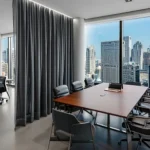 Conference room separated by grey fabric partition curtains for office with city skyline views in the background.