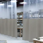 Beige and clear vinyl curtain wall dividing the glazing zone from pottery wheels and worktables in a ceramic classroom