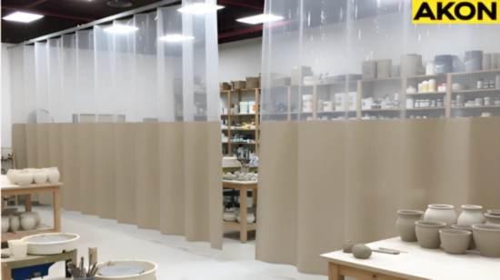 Beige and clear vinyl curtain wall dividing the glazing zone from pottery wheels and worktables in a ceramic classroom
