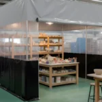 Black and gray insulated vinyl enclosure creating a controlled glazing room inside a large pottery production studio