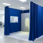 Blue curtain booth with a viewing window containing spray debris inside a bright industrial room