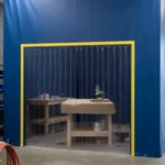 Blue vinyl spray booth enclosure with a clear strip door providing a contained workspace for spraying projects