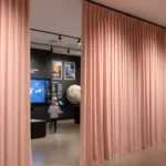 Blush fabric curtain walls creating separate exhibit zones in a museum, balancing style with acoustic and light control