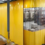 Bright yellow industrial curtain wall separating storage and brewing zones from customer seating area