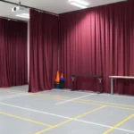 Burgundy fabric training curtains dividing an indoor safety training room into multiple confined-space practice zones with equipment organized nearby