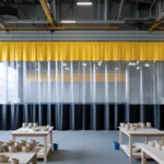 Clear vinyl curtain wall with yellow valance and black lower panels creating a glazing room inside a ceramics workshop