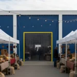 Large blue vinyl entry backdrop with clear strip door used for crowd flow and booth organization at an outdoor farmers market