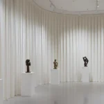 Museum exhibit divider curtains separating curved gallery walls with bronze sculptures on display