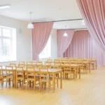 Soft pink Curtains for Camps and Retreat Centers used to divide a bright dining hall with wooden chairs and tables