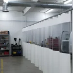 White and clear vinyl divider panels forming a spray foam spraying area along a workshop bay