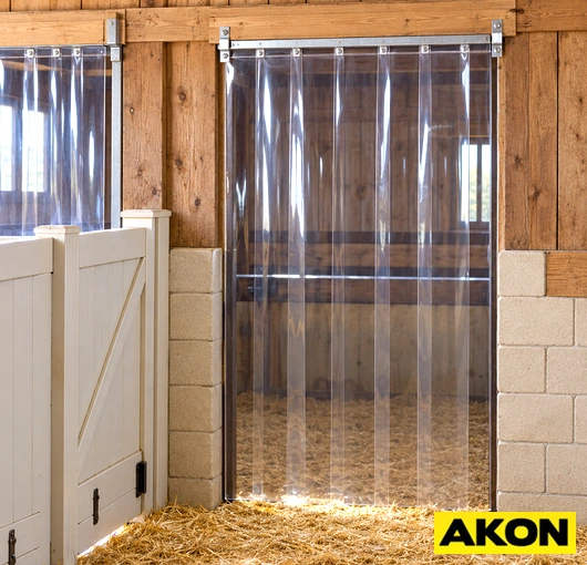 Clear PVC strip curtain installed across a barn door or stable animal opening to separate interior and exterior areas.