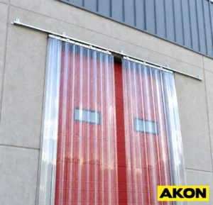 A sliding strip curtain pushed to the side of a doorway opening, allowing clear passage in an industrial facility.