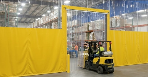 Forklift driving through a freestanding strip door with a yellow steel frame in a yellow warehouse curtain wall